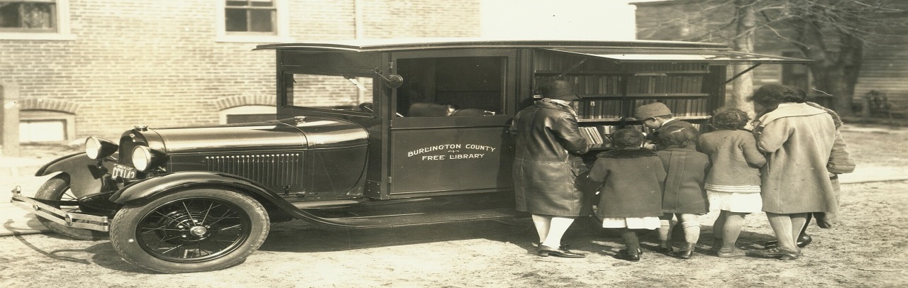 Burlington County Free Library Book Mobile in sepia with children and women looking at books on its side. 